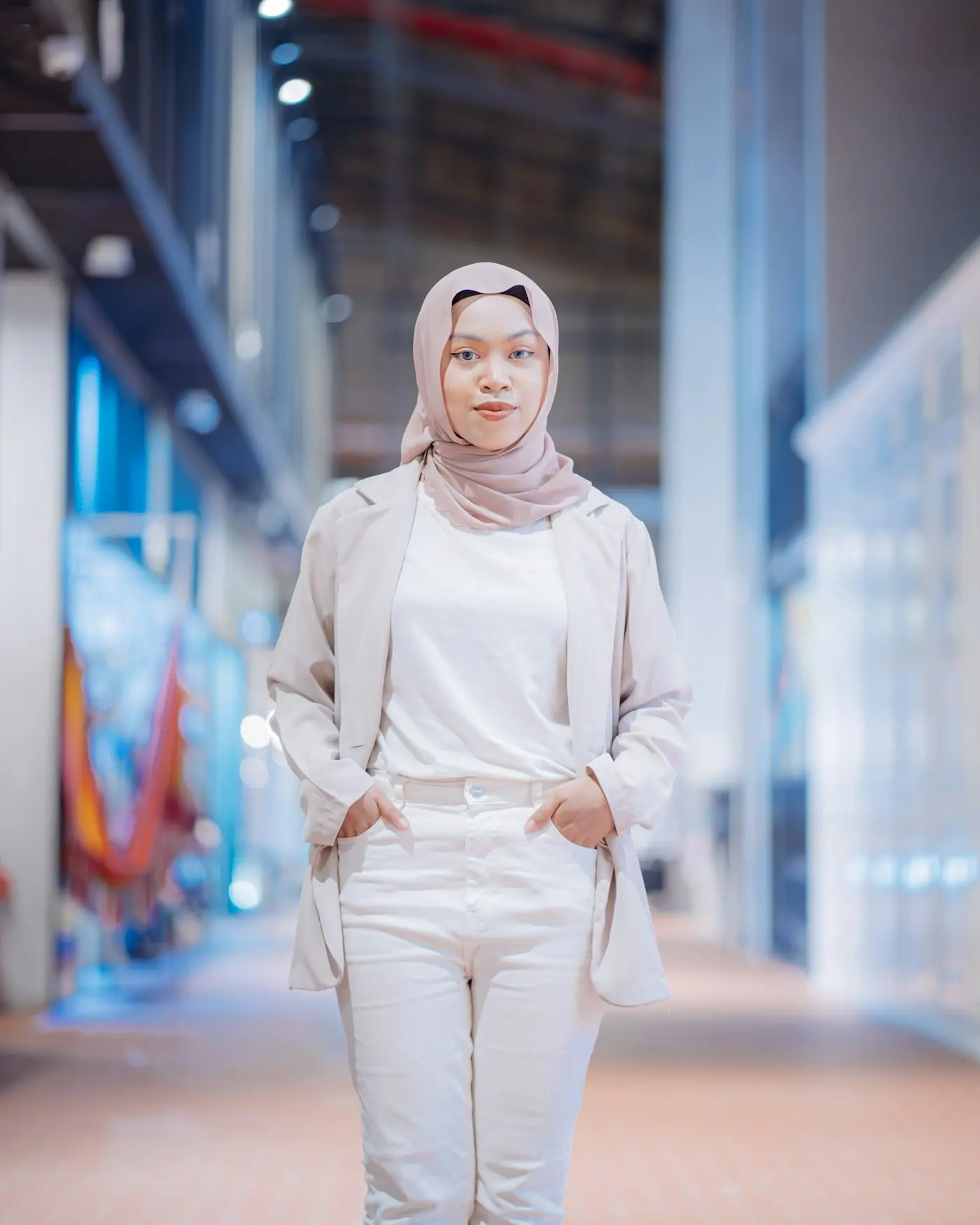 Seorang wanita bertudung dan berblazer tersenyum di koridor pejabat moden yang terang